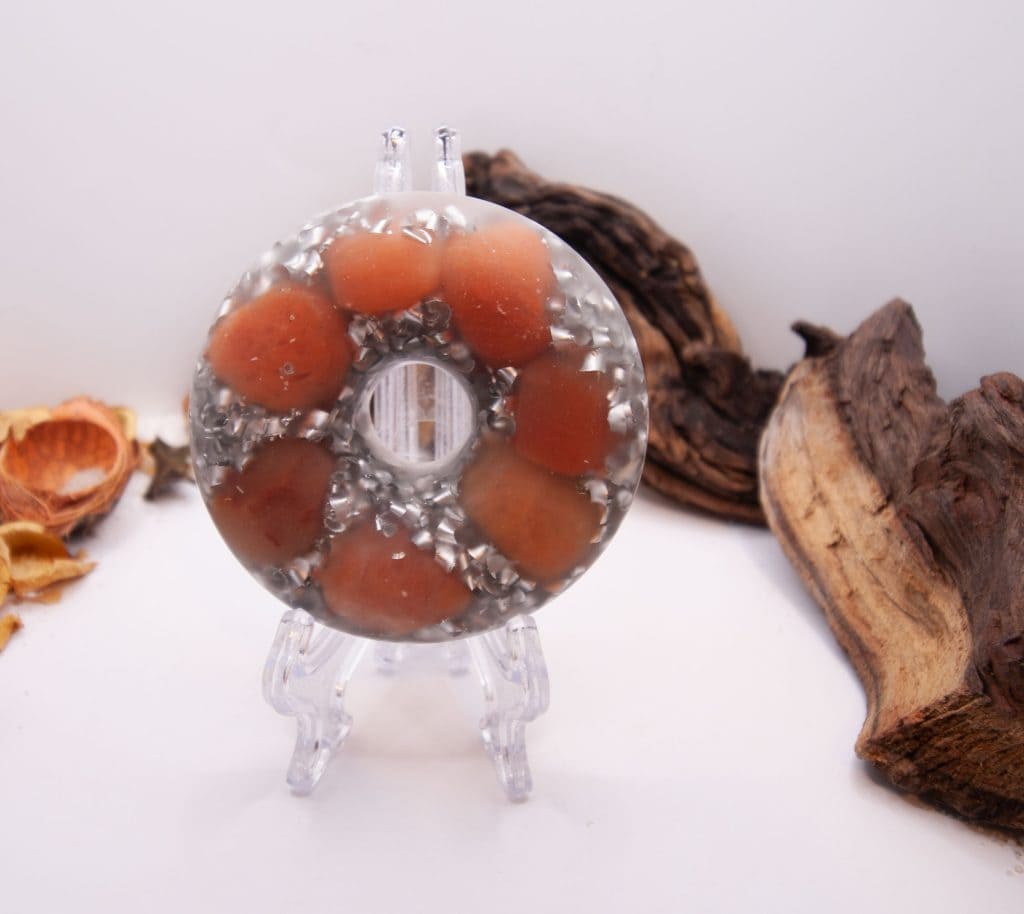 Epoxy resin case in the shape of a Torus on a plastic stand. Inside are Peach Aventurine, Quartz Crystals & Quartz Granite Granules, along with Aluminium shavings